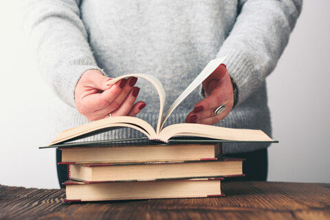 Young woman turning pages of old book on wooden table in antique