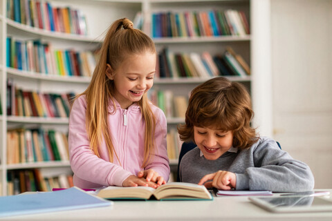 Happy caucasian primary school children reading book together in